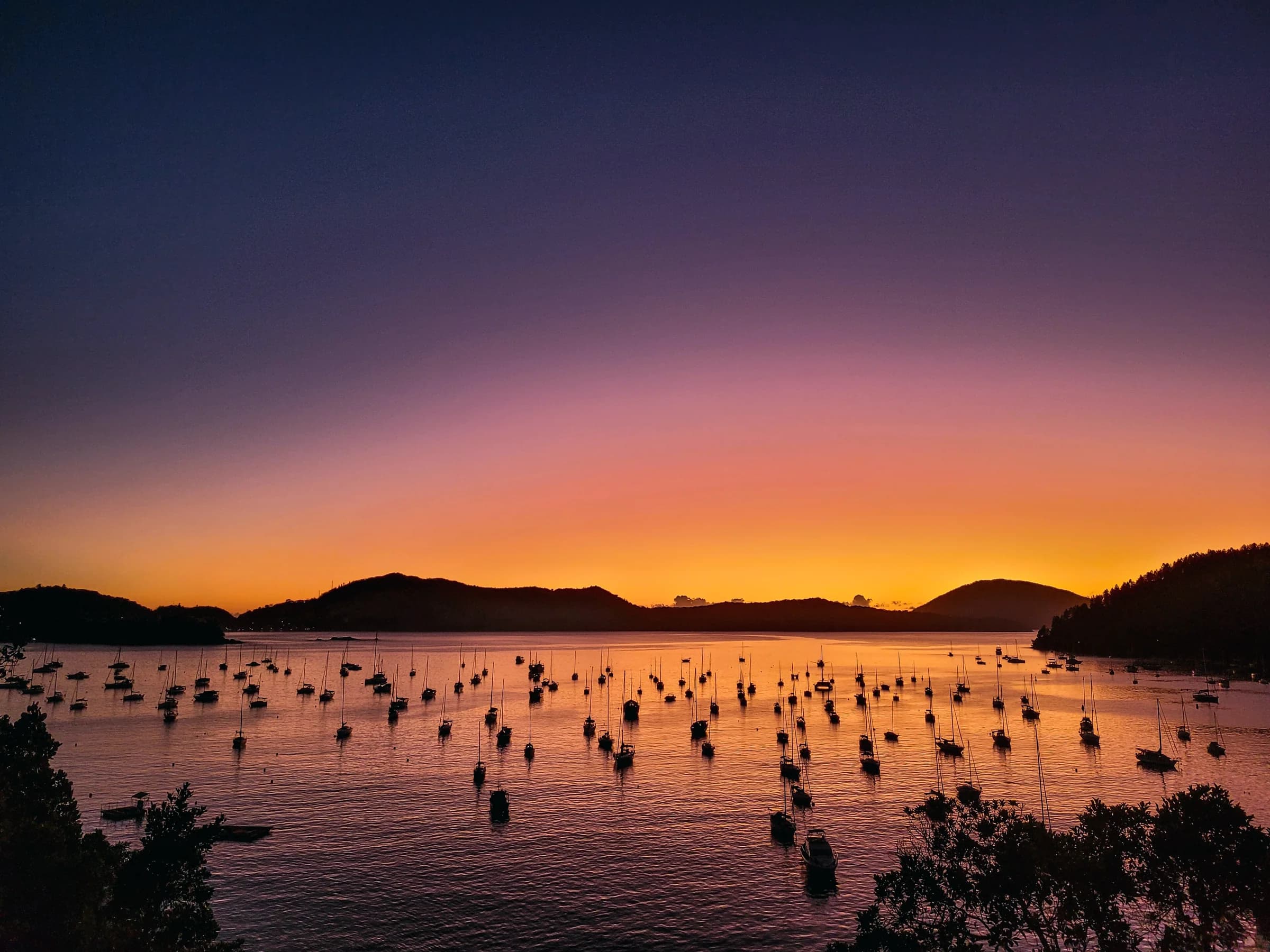 Amanhecer dourado no Saco da Ribeira, em Ubatuba, com barcos ancorados e ilhas ao fundo